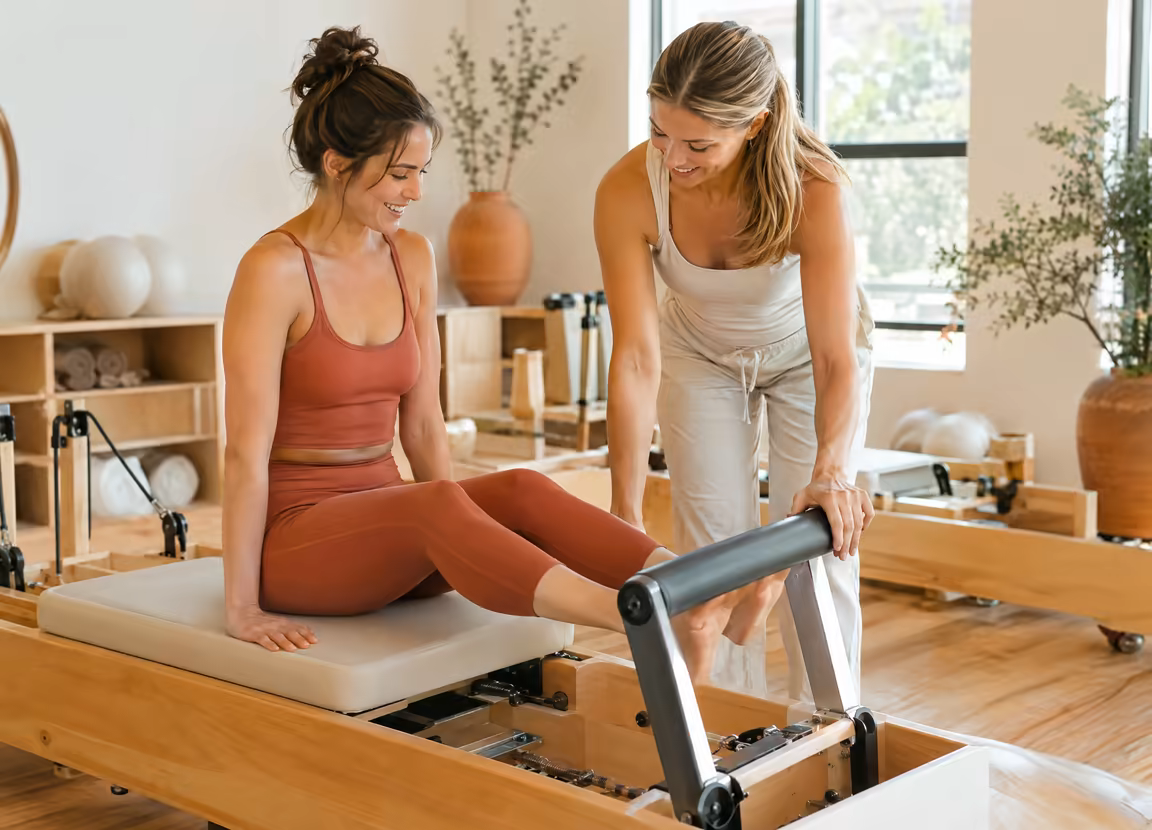 An instructor adjusting a beginner's footbar on a reformer
