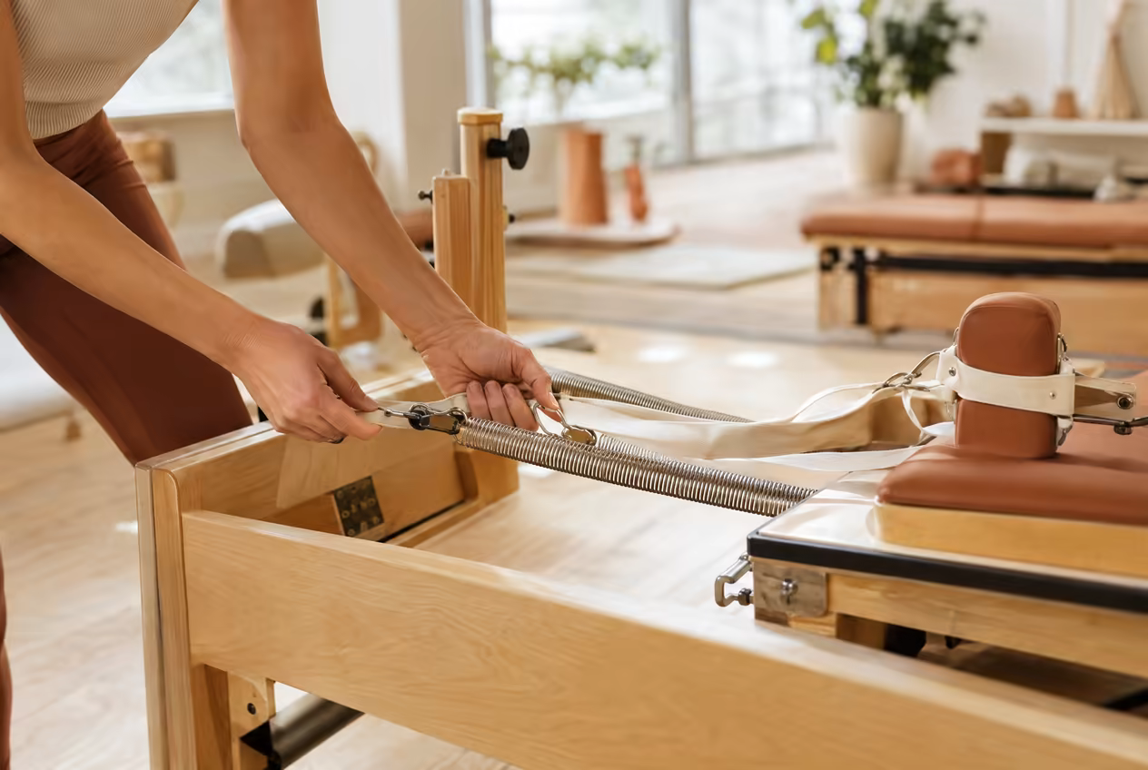 Hands adjusting the spring tension on a wooden reformer